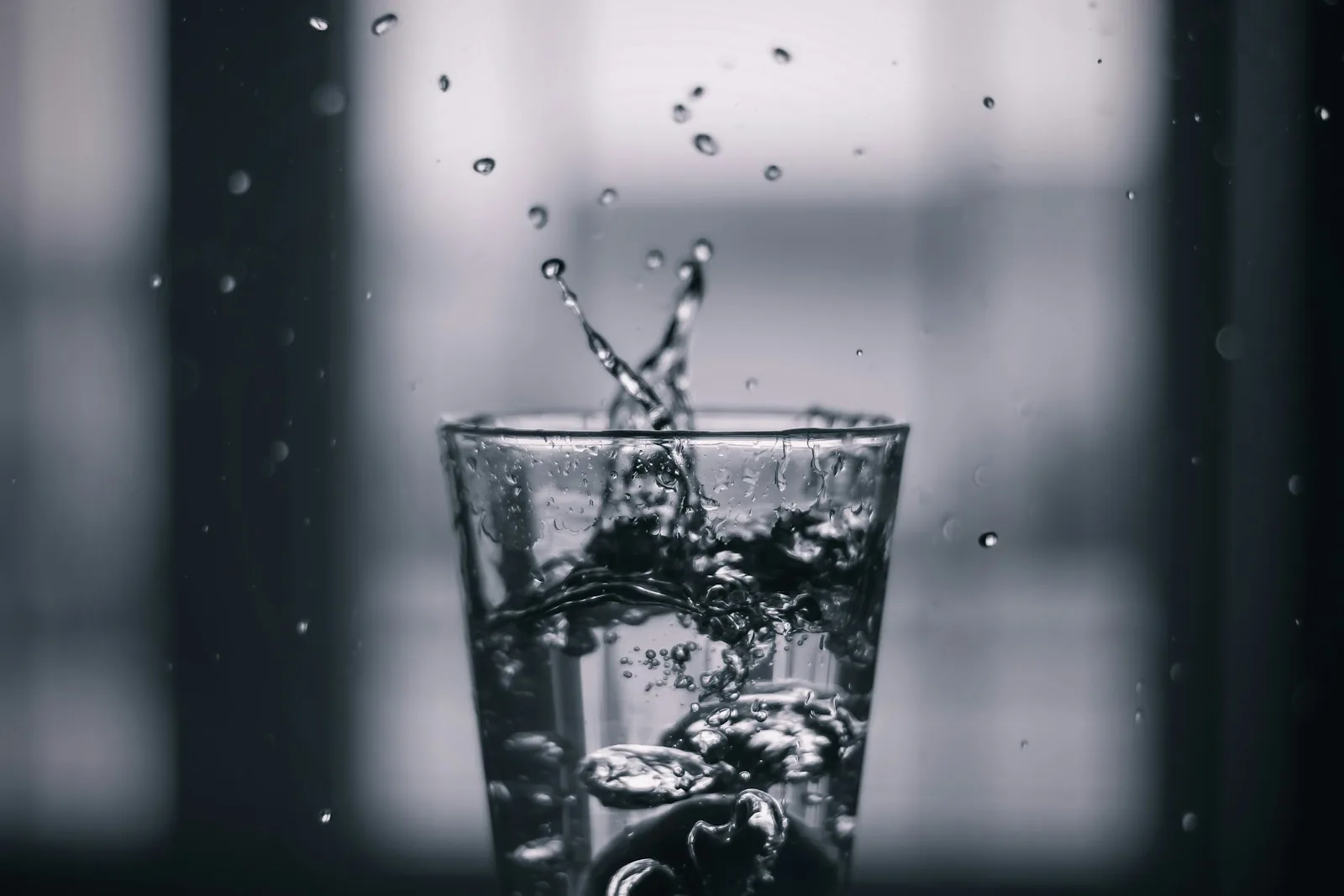 Water being poured into a clear glass, with a splash and suspended droplets